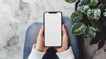 Mockup a person hands holding a smartphone with blank white screen while sitting on the floor at home photo