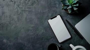 Top view of modern workspace with laptop, smartphone and plant on dark table photo