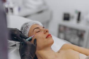 A professional beautician injects Botox into the face of a young woman photo
