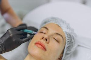 A professional beautician injects Botox into the face of a young woman photo
