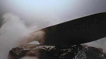 An expensive exclusive knife with a premium design in clouds of smoke among the stones. Slowly rotates in front of the camera. video