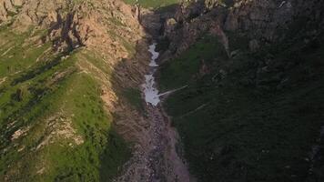 A drone flies over a mountain ravine with ice. There are trees and bushes around. Sunny Spring Day video