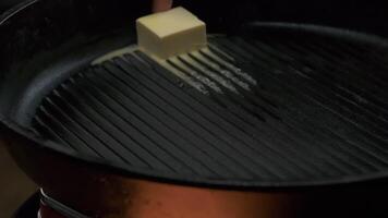 a piece of butter is melted in a frying pan, close up video