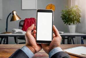 Mobile phone with blank screen in a businessman hands on an office table background. photo