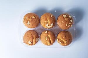 Freshly baked almond muffins in a transparent plastic tray on a white background. photo