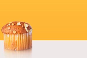 Delicious almond topped cupcake muffin with reflection on white table with yellow background. Template for product presentation. photo
