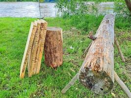 Planks and logs lie on the grass by the river, seasoning for building a raft. photo
