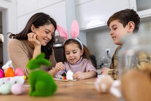 Mother, son and daughters are painting eggs. Happy family are preparing for Easter. Cute little child girl wearing bunny ears. photo