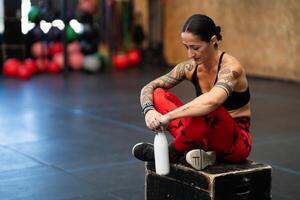 cansado mujer mirando abajo sentado en un caja en gimnasio foto
