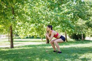 A woman is doing squats in a green park, showing an active and determined approach to fitness and health photo
