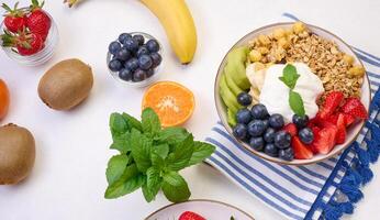 Granola with strawberries, kiwi, banana and blueberries in a round plate on a white table. photo
