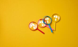 Plastic multi-colored magnifying glasses with a question mark on a yellow background photo