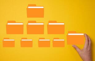 Hand holds a yellow folder over a yellow background with several folders. photo