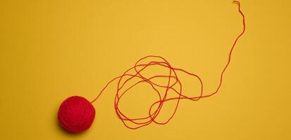 A ball of red woolen threads on a yellow background photo