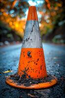 Orange traffic cone covered with mud on the road and trees in the background photo
