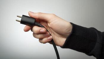 A person holding a black electrical plug on a gray background. The close-up image focuses on the hand and the plug. photo