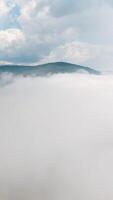 Top view of thick clouds with mountain peak on horizon. Schot. Flying in cloudy sky with dense clouds from top of mountain. Landscape of top of green mountain on horizon among white clouds video