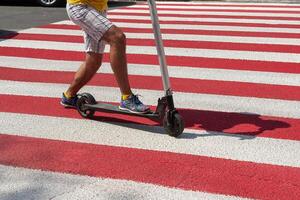 Detail of a man riding a non-electric kick scooter in a crosswalk photo