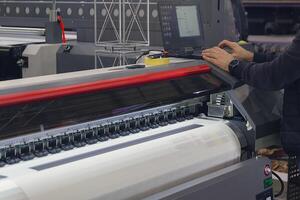 A man adjusts the printing process on a large format printing machine photo