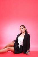full portrait of mature Asian woman in career office sitting elegantly wearing black suit, hands to thighs and floor, for corporate, fashion, commercial, agency content photo