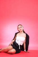 full portrait of young Asian career office woman sitting elegantly covered in black jacket, hands to thighs and floor, for corporate, fashion, commercial, agency content photo