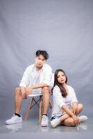 elegant men and women are posing sitting in front of the camera while the ladder holding the calves facing forward in the indoor. fashion promotion couple photo session in gray background studio