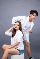 elegant men and woman posing standing in front of the camera while the ladder holding the hair in the indoor. fashion promotion couple shirt photo session in gray background studio
