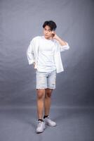 elegant asian man posing standing head tilted in front of camera while hands back indoors. fashion promotion man shirt photo session in the gray background studio