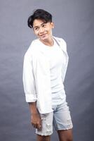 elegant asian man posing standing tilted body forward in front of the camera while his stairs back indoors. fashion promotion man shirt photo session in the gray background studio