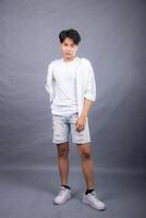 elegant asian man indonesian posing standing in front of the camera with his hands back indoors. fashion promotion man shirt photo session in the gray background studio