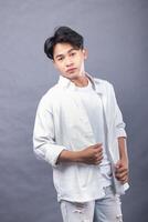 elegant asian man posing with his head held high in front of the camera while holding his shirt in his hand indoors. fashion promotion man shirt photo session in the gray background studio