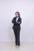 full body portrait of an adult Asian blue shirt office woman wearing a hijab standing at right angles smiling with arms crossed. Beautiful Muslim women use business, technology and fashion content photo