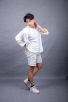 elegant asian man posing standing straight head to side in front of camera while hands back indoors. fashion promotion man shirt photo session in the gray background studio