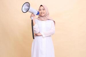 woman muslim asian in hijab looking at the camera smiling cheerfully holding a loudspeaker megaphone. Technology, broadcast and promotion concept photo