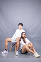 elegant men and women posing sitting in front of the camera while leaning back indoors. fashion promotion couple photo session in gray background studio