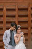 a pair of men and women in elegant poses standing with men arms embracing from behind while closing their eyes to the side wearing beautiful dresses in a park photo shot