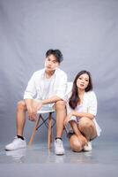 elegant men and women are posing sitting in front of the camera while the stairs are holding their knees facing forward in the indoor. fashion promotion couple photo session in gray background studio