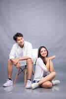 cheerful smiling man and woman posing sitting in front of camera while ladder holding each other indoors. fashion promotion couple photo session in gray background studio