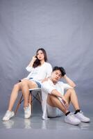 elegant men and women posing sitting in front of the camera while the ladder holding the hair facing forward in the indoor. fashion promotion couple photo session in gray background studio
