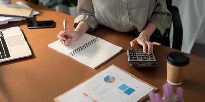 Businesswoman using laptop computer and working at office with calculator document on desk, doing planning analyzing the financial report, business plan investment, finance analysis concept photo