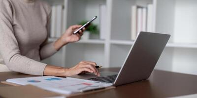 Businesswoman using laptop computer and working at office with calculator document on desk, doing planning analyzing the financial report, business plan investment, finance analysis concept photo
