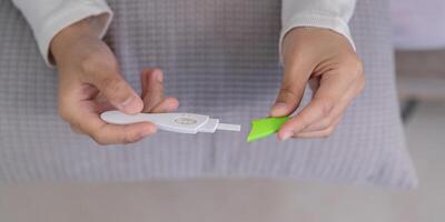 Close up of Hands Holding a Pregnancy Test Kit with a Pillow in the Background, Focus on the Abdomen Area photo