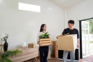 Happy Couple Moving into New Home Carrying Boxes and Plants in Bright Modern Living Room photo