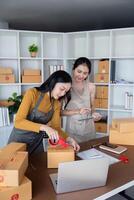 Friends Working Together to Sell Product Online, Packing Boxes and Using Laptop in Modern Home Office photo