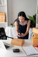 Young Woman Preparing Parcel Boxes for Online Business with Laptop and Calculator in Modern Workspace photo