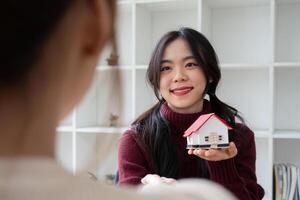 Smiling Real Estate Agent Holding a Model House, Promoting Home Sales or Home Insurance in a Modern Office Setting photo