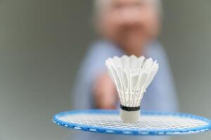 Selective focus of shuttlecock and badminton racket with blurred Asian senior sportswoman in background photo