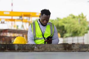 capataz trabajador utilizando móvil teléfono inteligente a el construcción sitio, ingeniero hombre toma un descanso en el prefabricado fábrica sitio foto