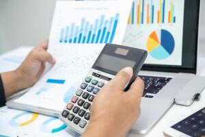 Asian accountant working and analyzing financial reports project accounting with chart graph and calculator in modern office, finance and business concept. photo