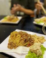 Indonesian food. noodles topped with chicken and dumplings. served on a square plate photo